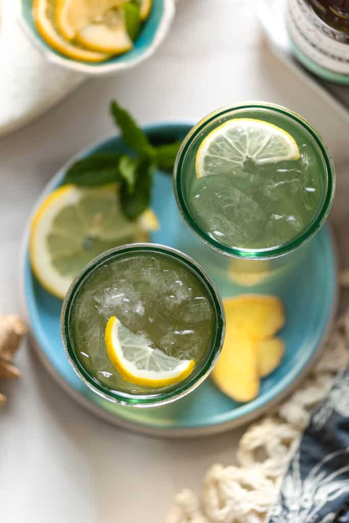 two glass of homemade switchel with crushed ice and lemon slices on a plate with fresh mint on the side