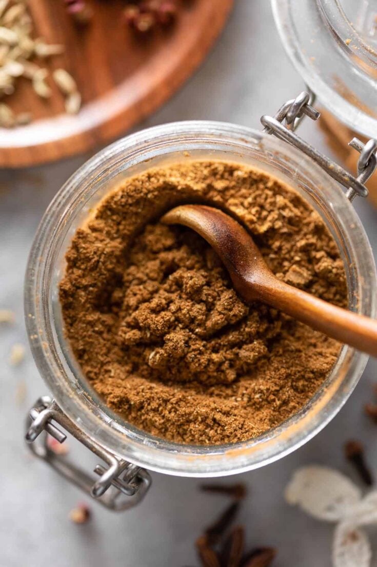 homemade Chinese five spice powder in a small storage jar with a wooden spoon