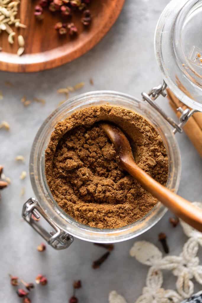 homemade Chinese five spice powder in a small storage jar with a wooden spoon