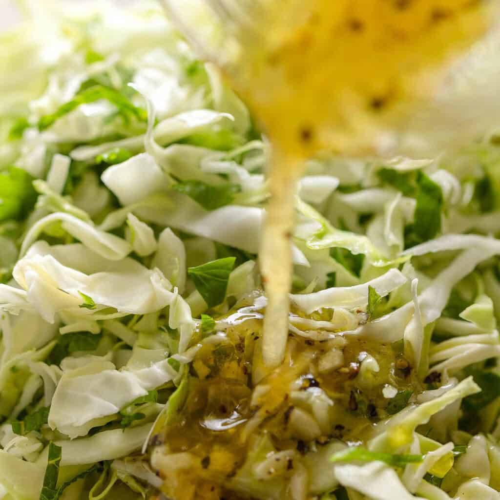 lemon vinaigrette pouring over a cabbage salad