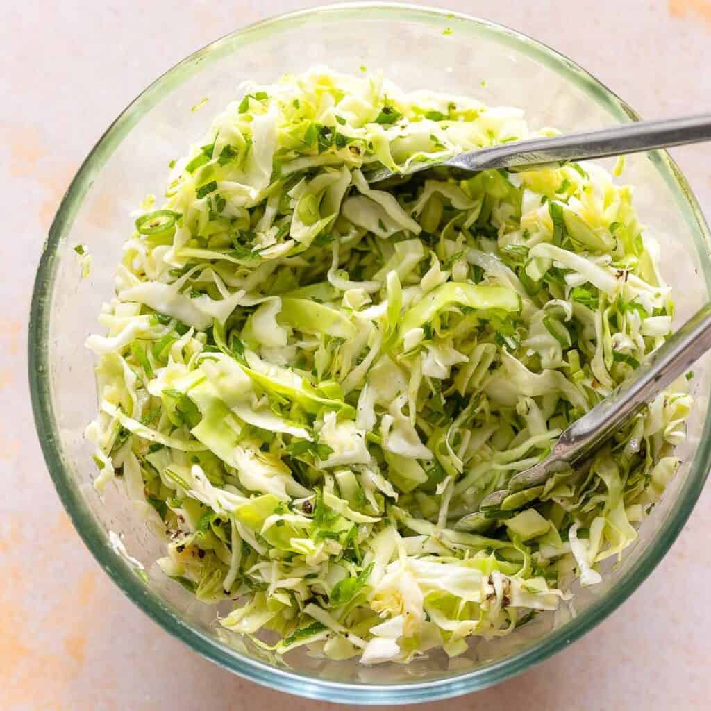 a bowl full of malfouf salad tossed together with a pair of tongs