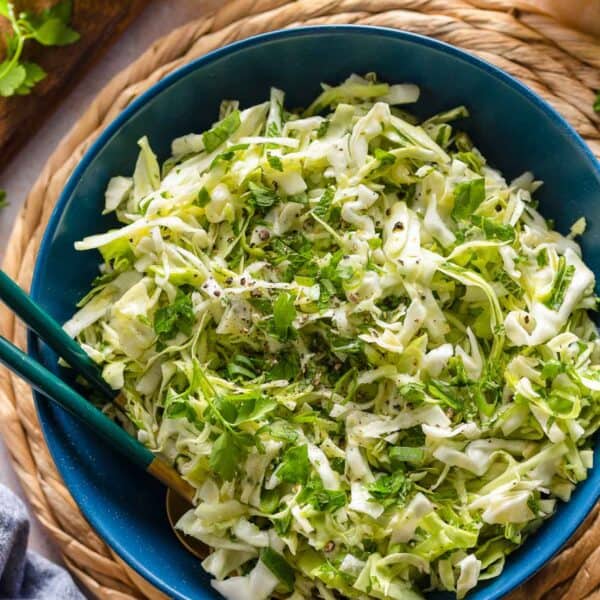 malfouf salad (lebanese cabbage slaw) in a salad bowl with a pair of serving forks surrounded by fresh lemons and herbs