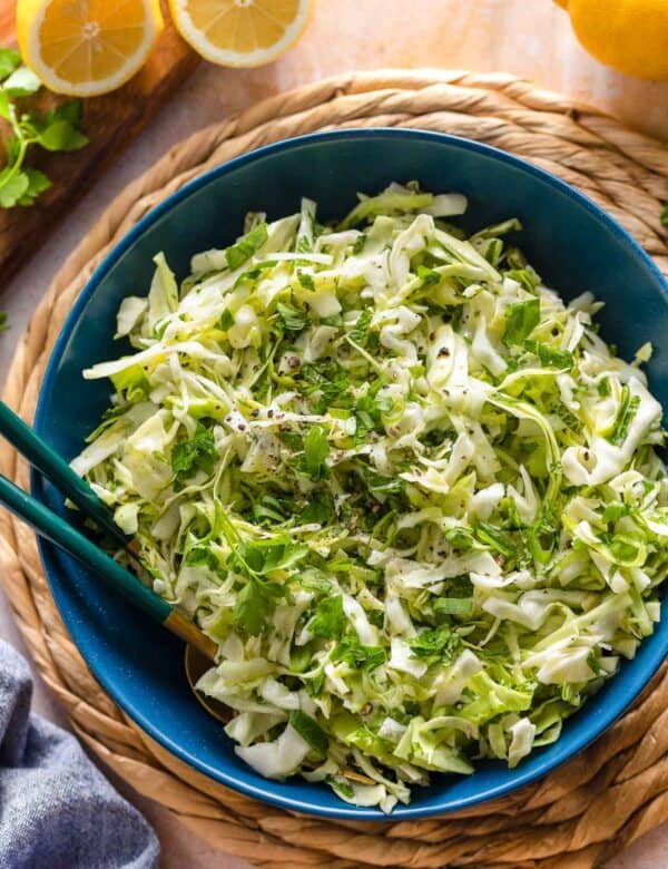 malfouf salad (lebanese cabbage slaw) in a salad bowl with a pair of serving forks surrounded by fresh lemons and herbs