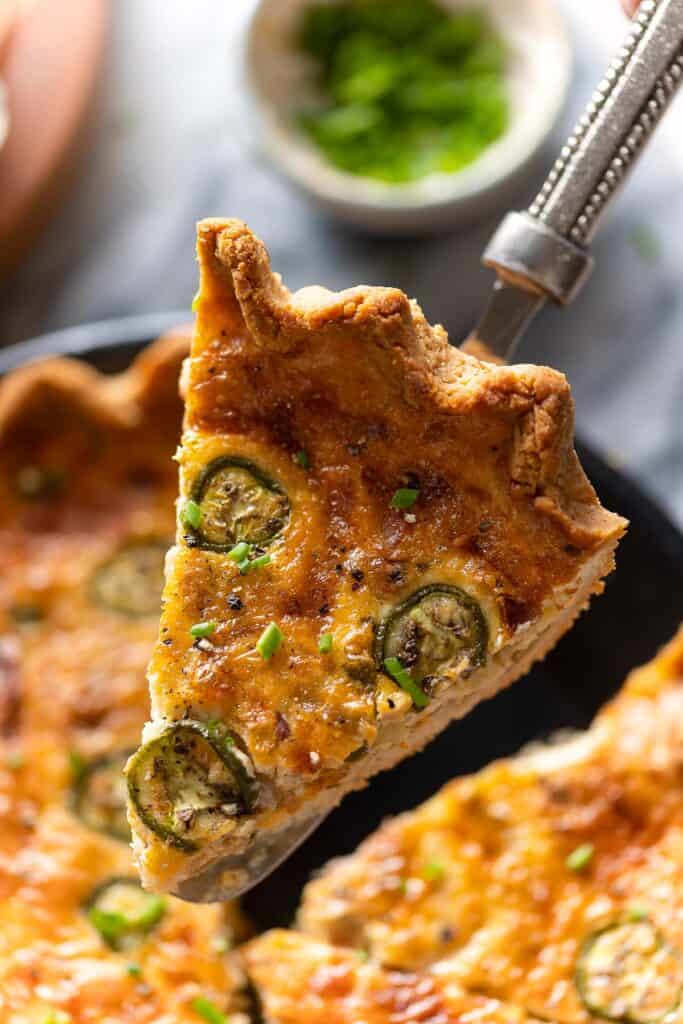 a serving spatula holding up a slice of Bacon & Cheddar Jalapeño Quiche tipped with fresh chopped chives