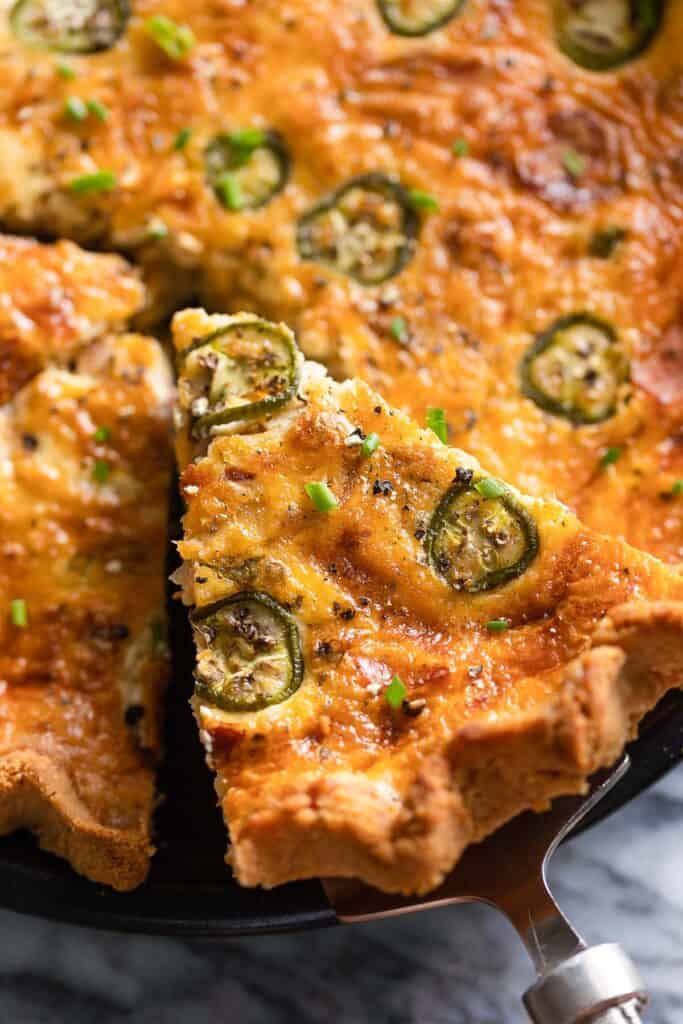 a serving spatula holding up a slice of Bacon & Cheddar Jalapeño Quiche tipped with fresh chopped chives