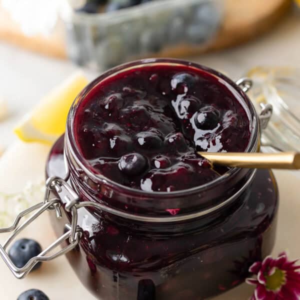 homemade blueberry filling for cakes and pies in a jar with a spoon surrounded by fresh berries