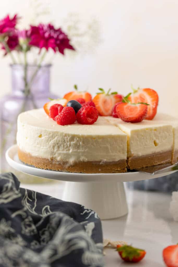 A cake knife about to pic up a slice of gluten free no bake cheesecake on a cake platter with fresh berries on top.