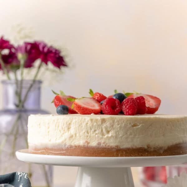 gluten free no bake cheesecake on a cake stand with fresh berries on top