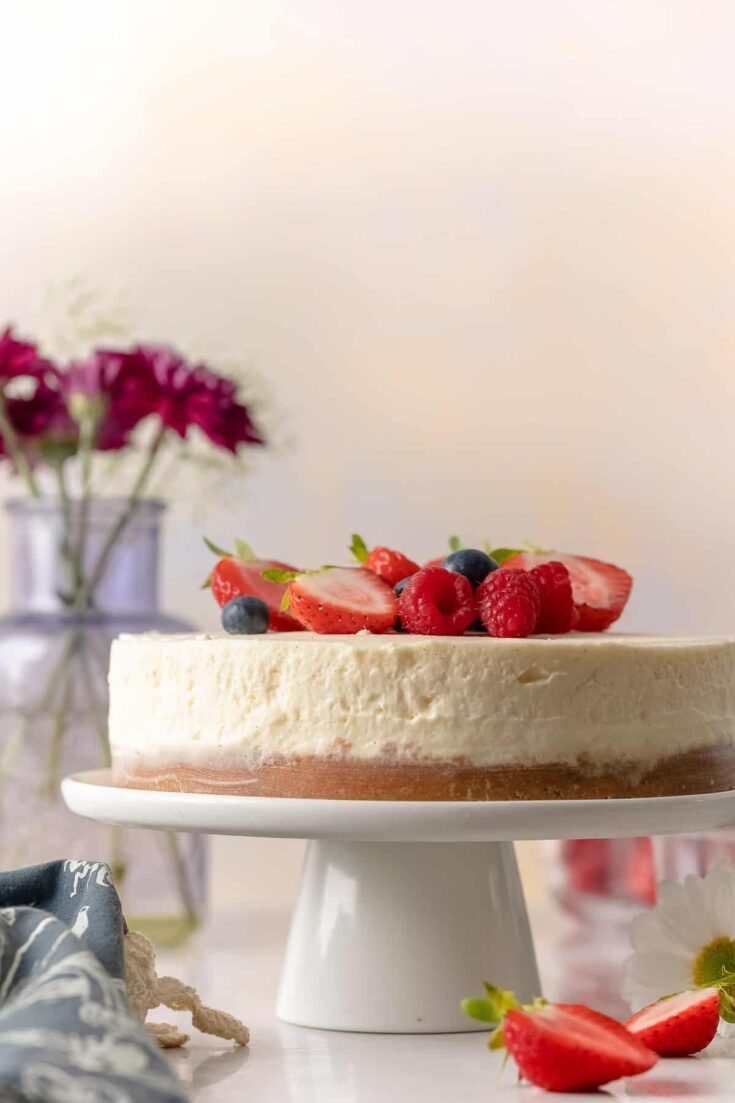 gluten free no bake cheesecake on a cake stand with fresh berries on top
