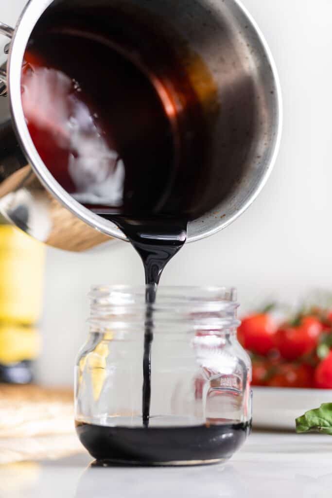 Homemade balsamic glaze pouring out of a sauce pan and into a small storage jar