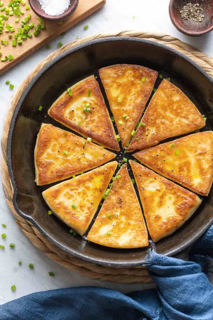 Eight slices of Irish potato bread in a skillet with fresh chives and black pepper sprinkled over top.