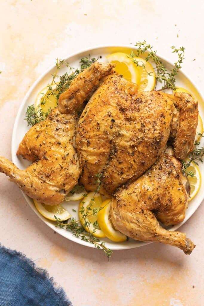 Spatchcocked Chicken on a plate with fresh thyme and lemon slices.