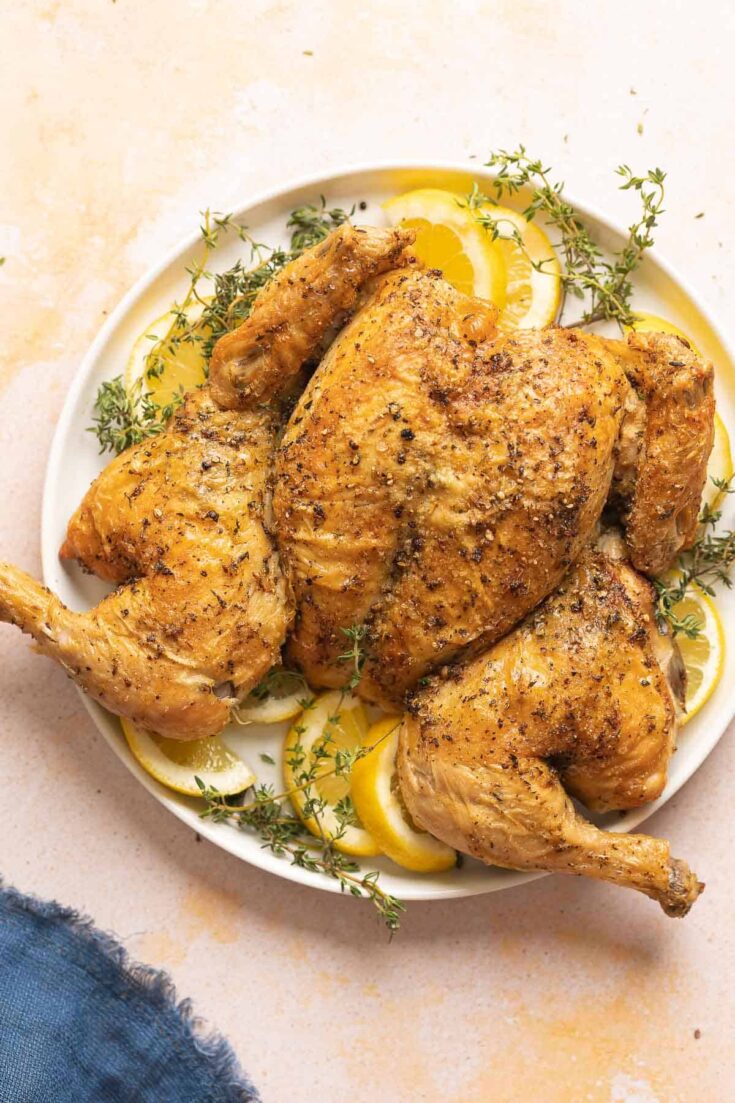 Spatchcocked Roast Chicken on a plate with fresh thyme and lemon slices.