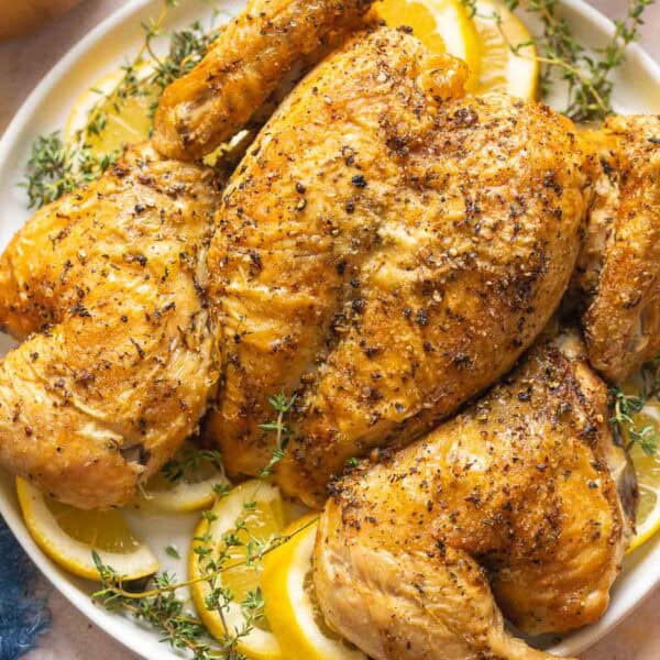 Spatchcocked Roast Chicken on a plate garnished with fresh thyme and lemon slices.