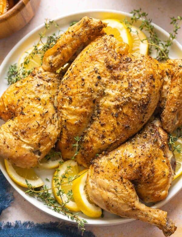 Spatchcocked Roast Chicken on a plate garnished with fresh thyme and lemon slices.
