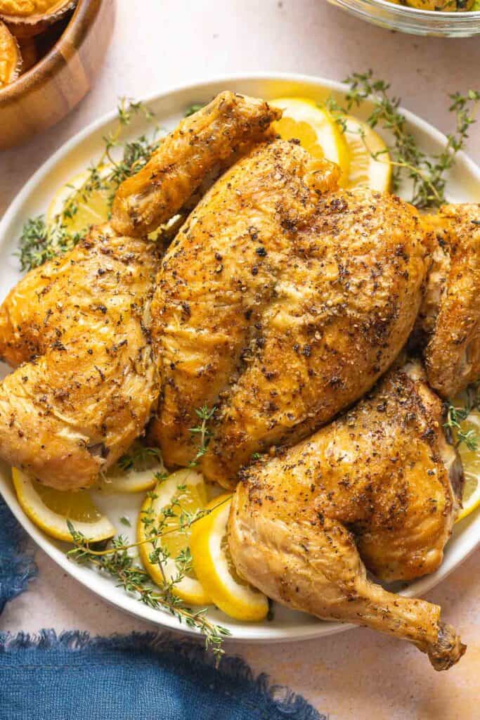 Spatchcocked Chicken on a plate garnished with fresh thyme and lemon slices.