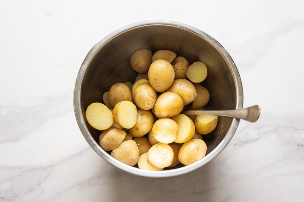 Boiled new potatoes in a mixing bowl with a mixed herb mixture underneath.