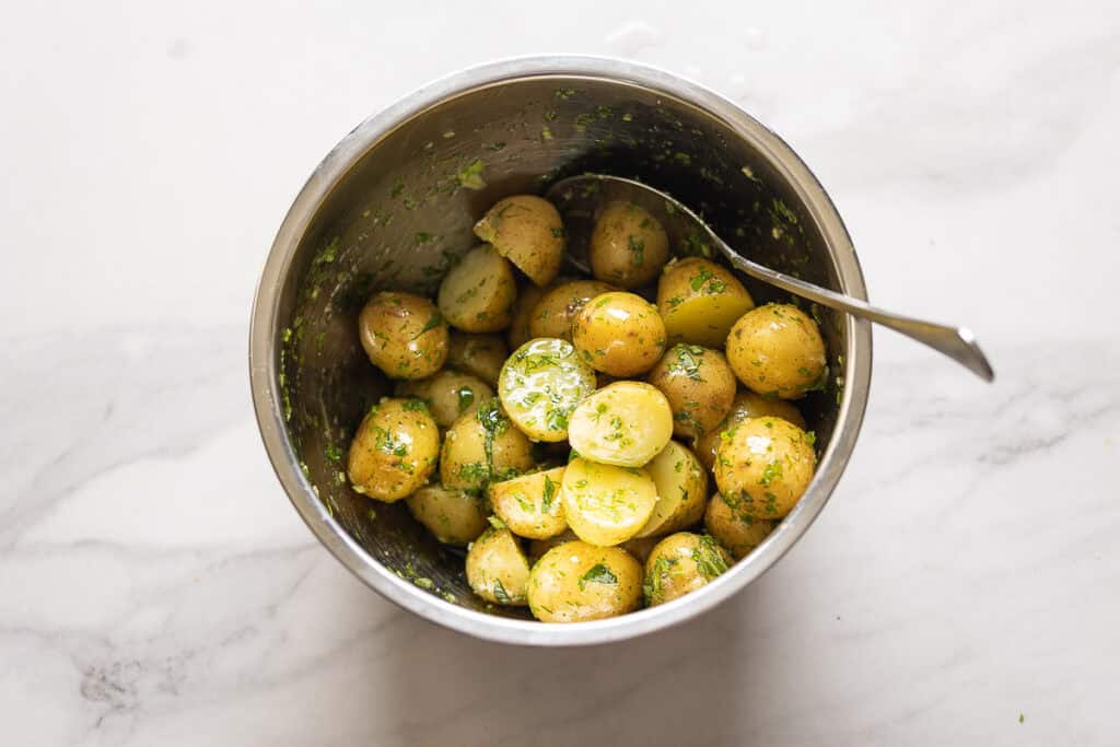 Boiled new potatoes tossed in a herb and olive oil mixture in a large mixing bowl.