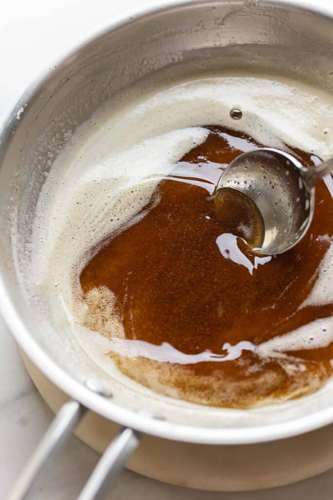 A spoon swirling brown butter in a stainless steel pan.
