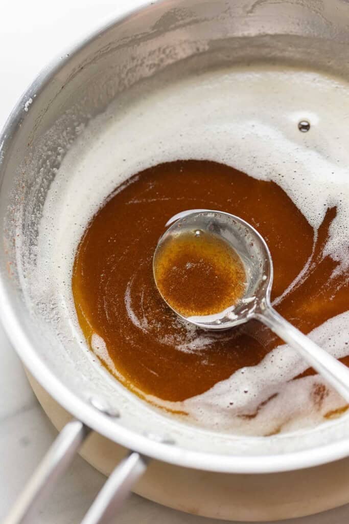 A stainless steel pan full of brown butter with a spoon holding up some of the toasted milk solids.