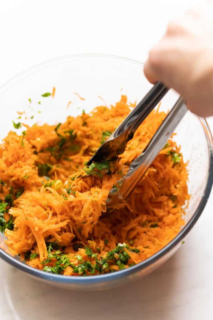 Grated carrots, chopped parsley and spring onions tossed together in a dressing with a pair of kitchen tongs to make a French Carrot Salad.