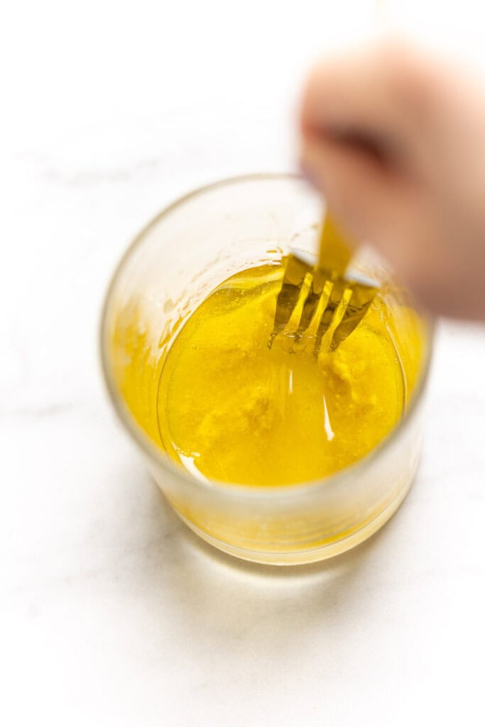 A lemon and olive oil dressing mixing together in a small cup.