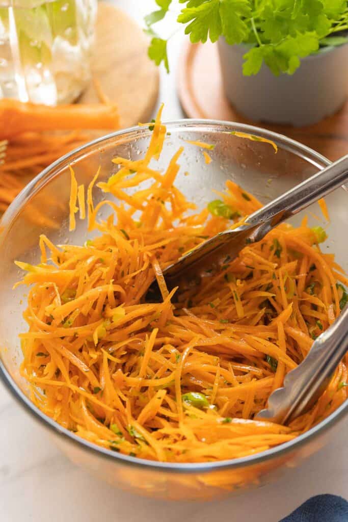 French Carrot Salad in a mixing bowl with kitchen tongs to toss the salad.