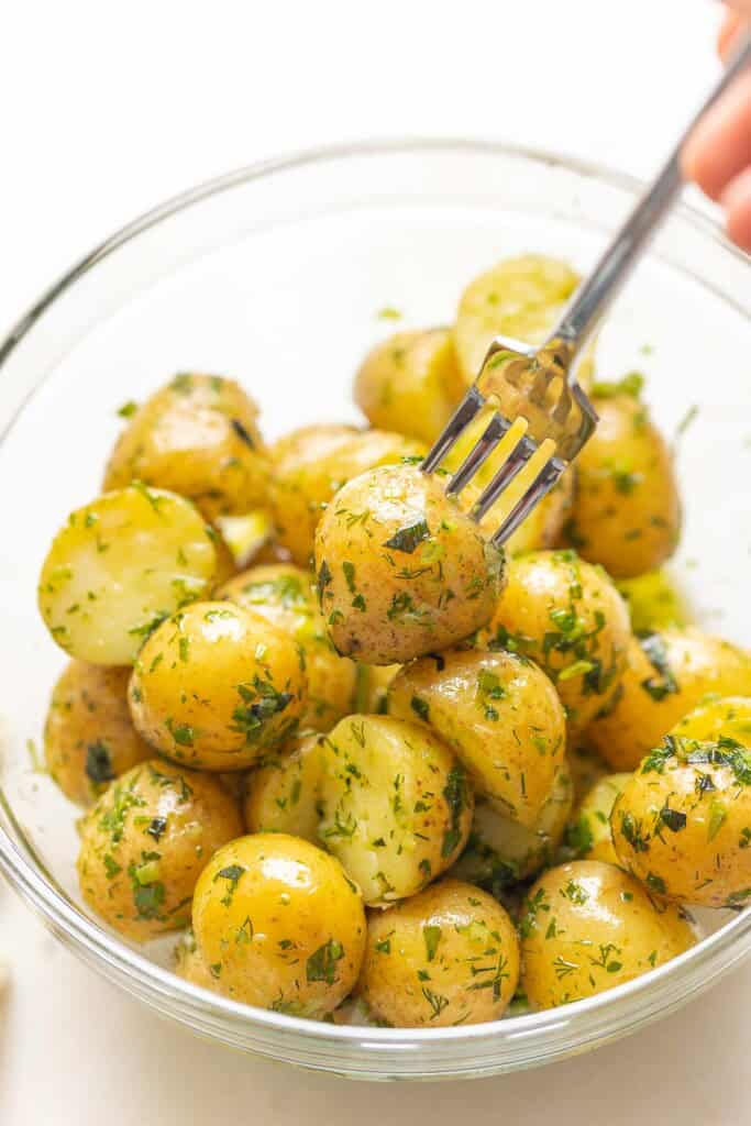 A fork piercing a boiled potato tossed in herbs and olive oil