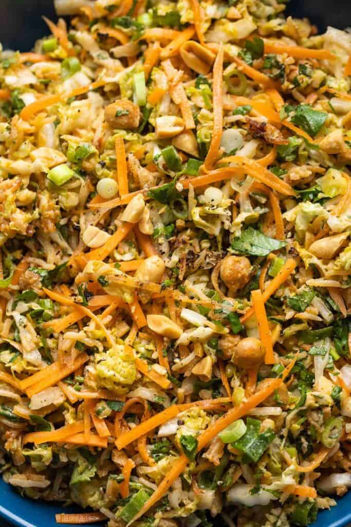 A crunch salad made up of: shredded cabbage, carrots, spring onion, herbs and peanuts in a peanut dressing. Fresh cilantro, chopped peanuts and spring onions in the back.