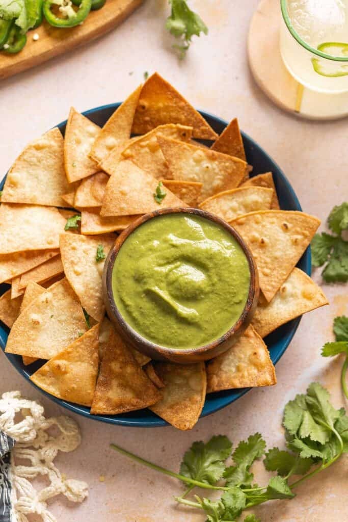 Jalapeño Zucchini Salsa  in a dip bowl on a plate with tortilla chips surrounded by fresh cilantro.