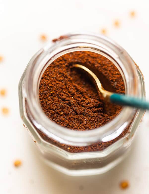 Homemade Ancho Chili Powder in a spice jar with a spoon.