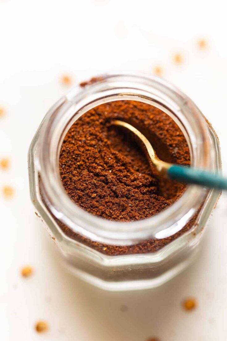 Homemade Ancho Chili Powder in a spice jar with a spoon.
