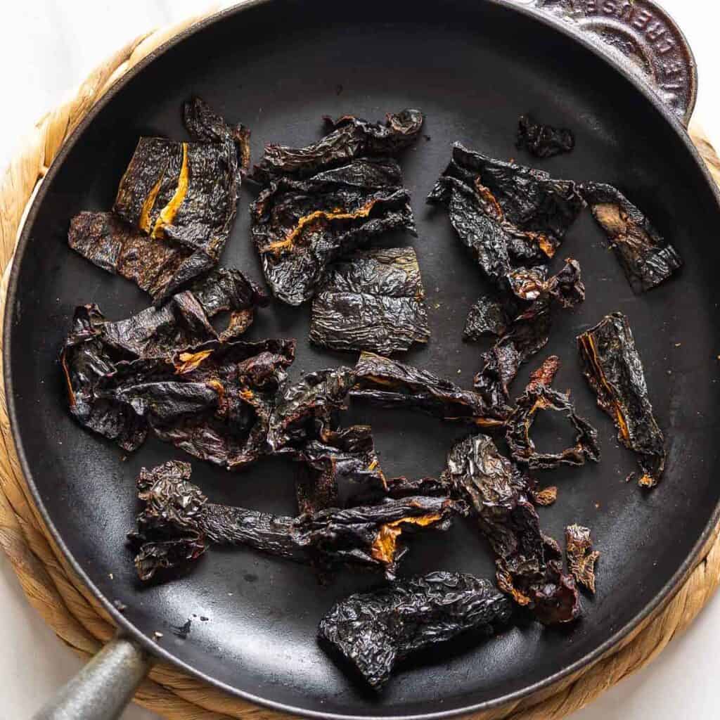 Whole, dried ancho chiles toasting on a cast iron skillet.