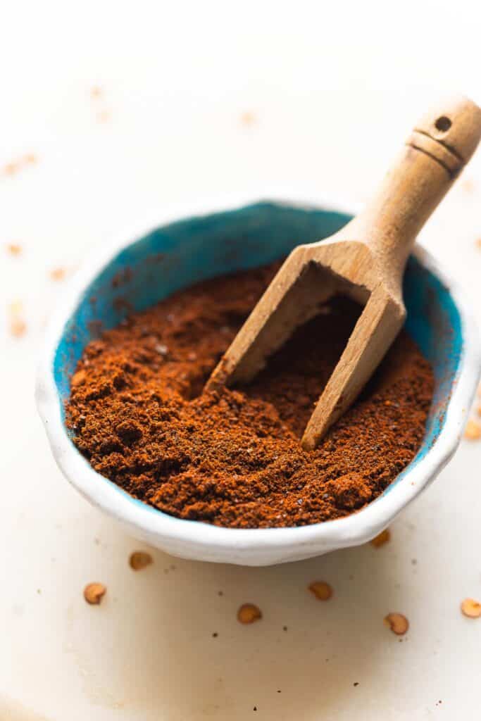 Homemade ancho chile powder in a small bowl with a wooden scoop.