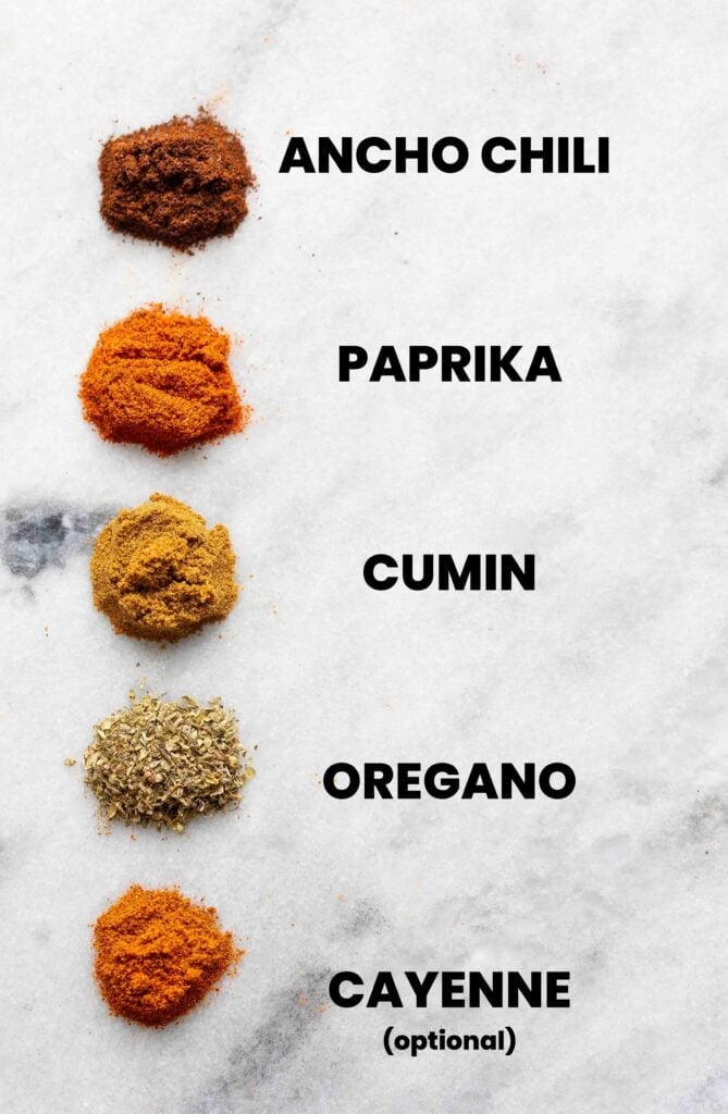 Low FODMAP chili powder spices on a marble surface: ancho chili, paprika, cumin, oregano and cayenne (optional)