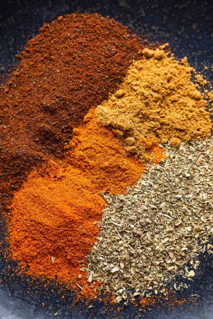 Low FODMAP Chili Spices on a plate: ancho chili powder, oregano, paprika, cayenne and cumin