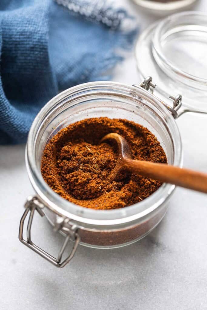 Homemade Low FODMAP Chili Spice in a small storage jar with a wooden spoon.