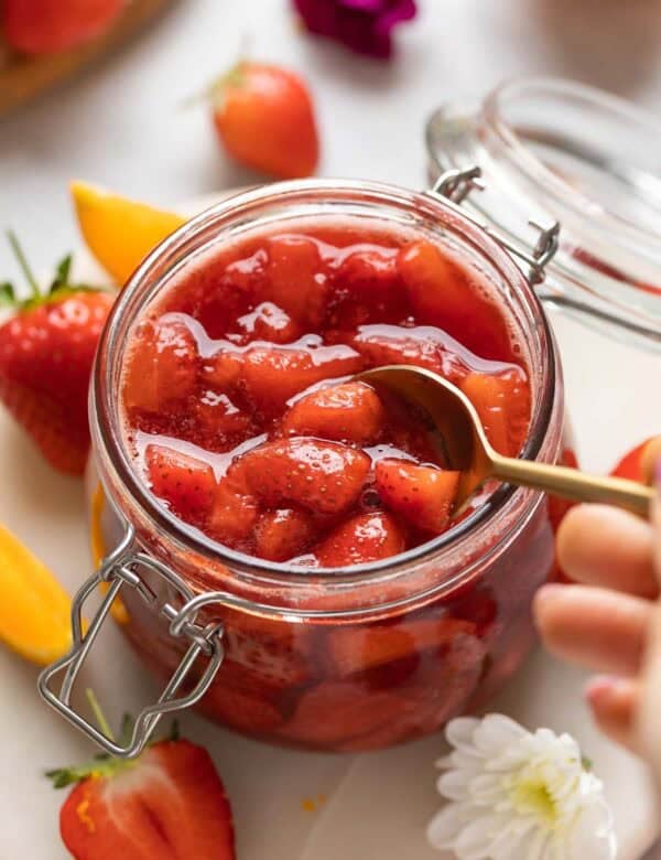 Strawberry compote in a storage jar getting stirred with a spoon.