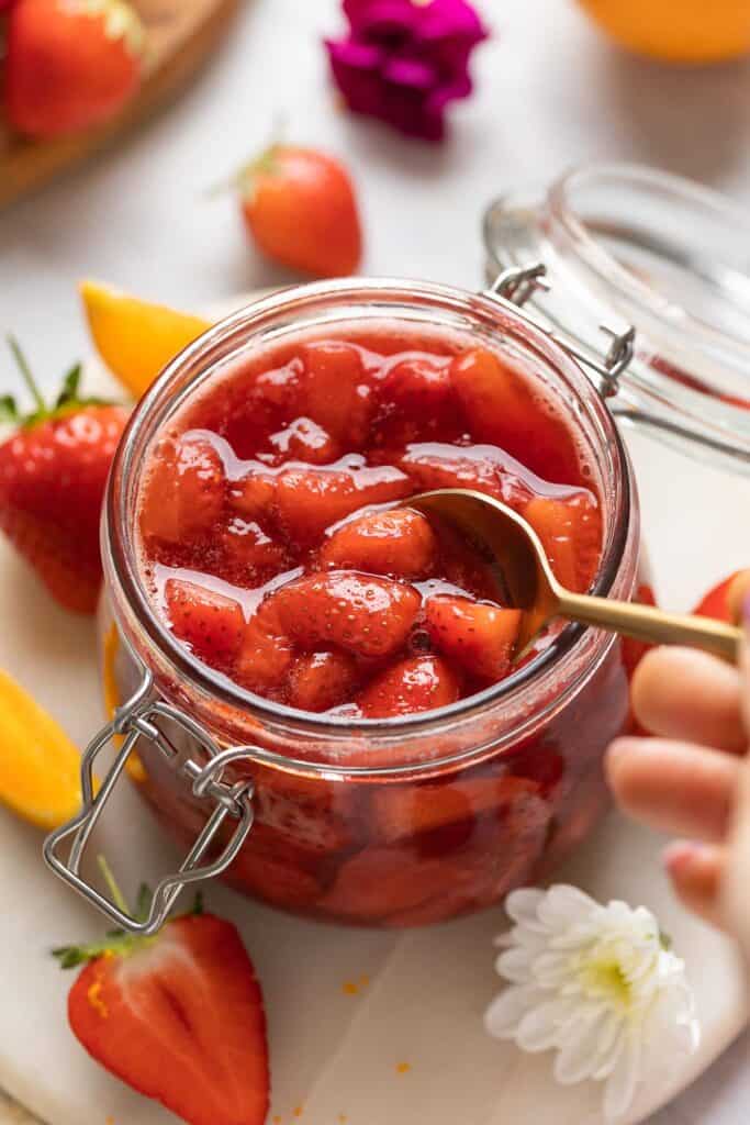 Strawberry compote in a storage jar getting stirred with a spoon.