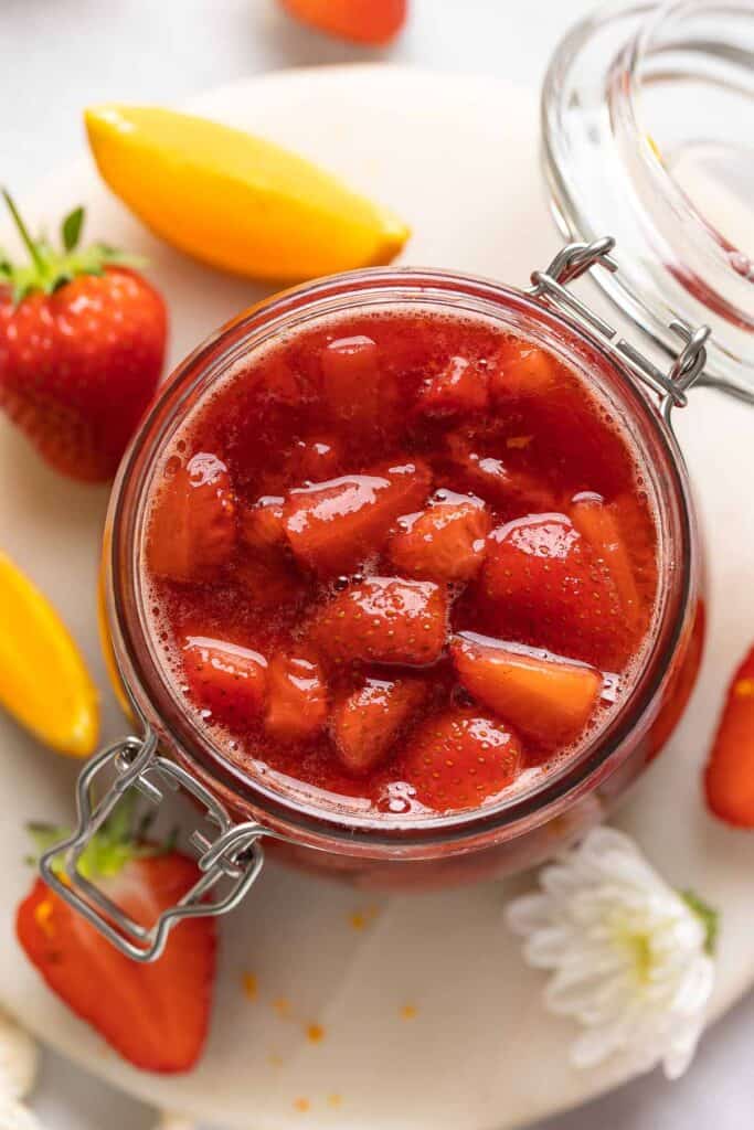 Strawberry compote in a storage jar with oranges and strawberries.