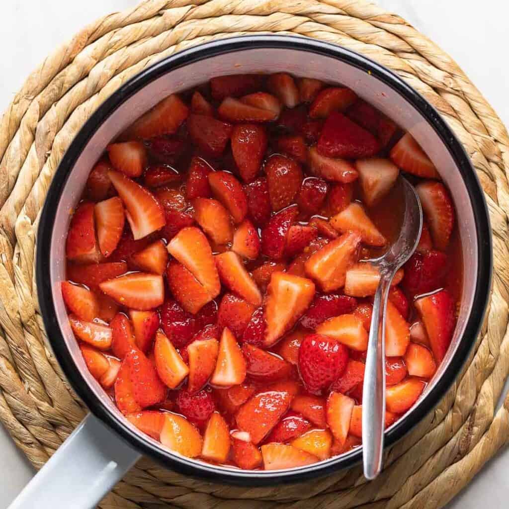 A saucepan full of simmering strawberries and compote ingredients