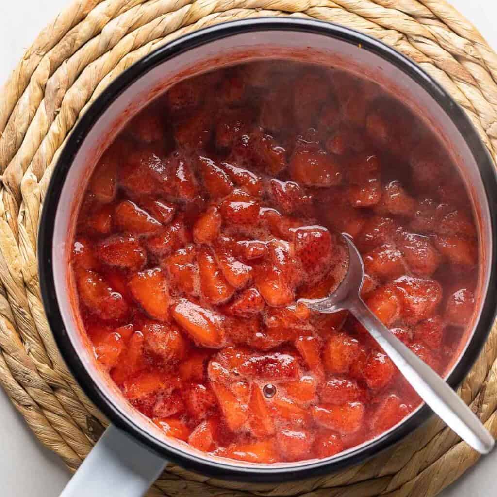 Fresh strawberry compote in a sauce pan with a spoon.