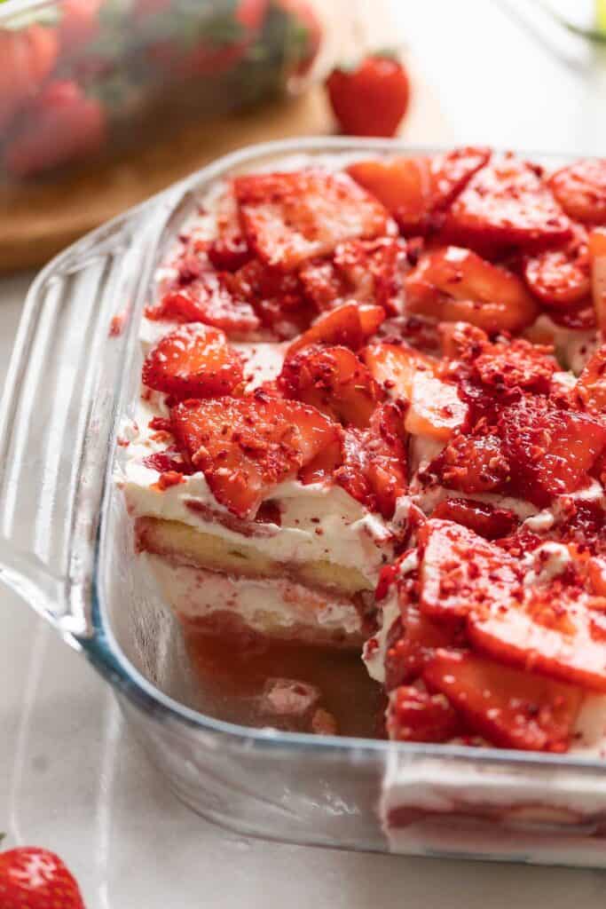 Strawberry shortcake tiramisu in a baking dish with a cake piece missing from the dish.