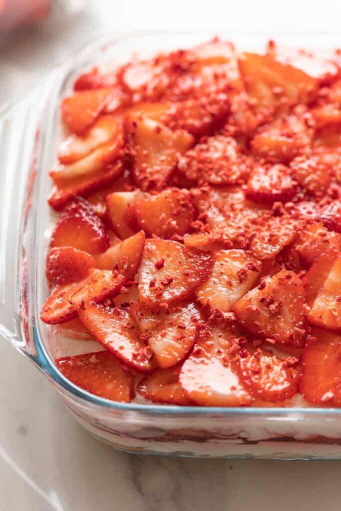 Strawberry shortcake tiramisu in a glass baking dish with fresh, sliced strawberries and dried strawberries on top.