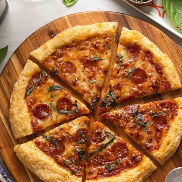 Homemade Gluten Free Cheese & Pepperoni Pizza on a wooden pizza tray topped with fresh basil.