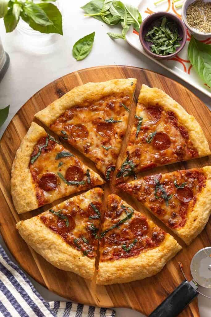 Homemade Gluten Free Cheese & Pepperoni Pizza on a wooden pizza tray topped with fresh basil. 