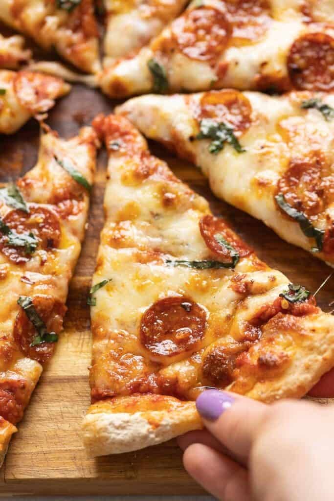 A hand grabbing a homemade gluten free cheese & pepperoni pizza slice.