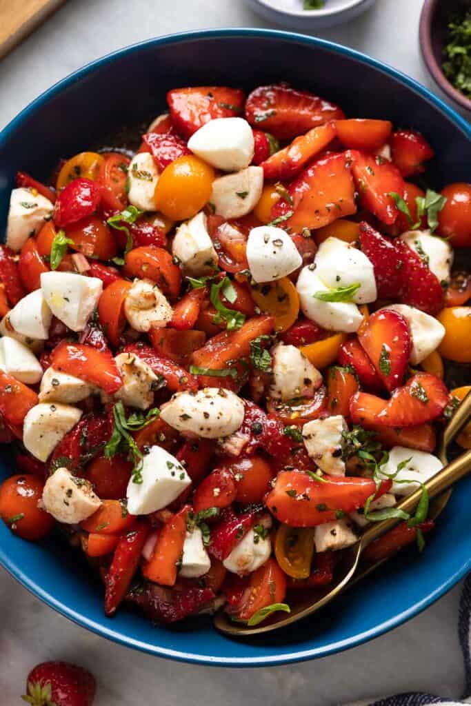 A Strawberry Tomato Balsamic Salad made with sliced strawberries, cherry tomatoes, mozzarella and fresh mint, basil and black pepper.