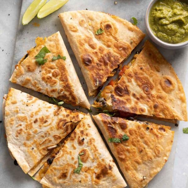 Two Sweet Potato & Black Bean Quesadillas arranged in circle and cut into 6 wedges on serving board with fresh cilantro and bowls of salsa on the side.