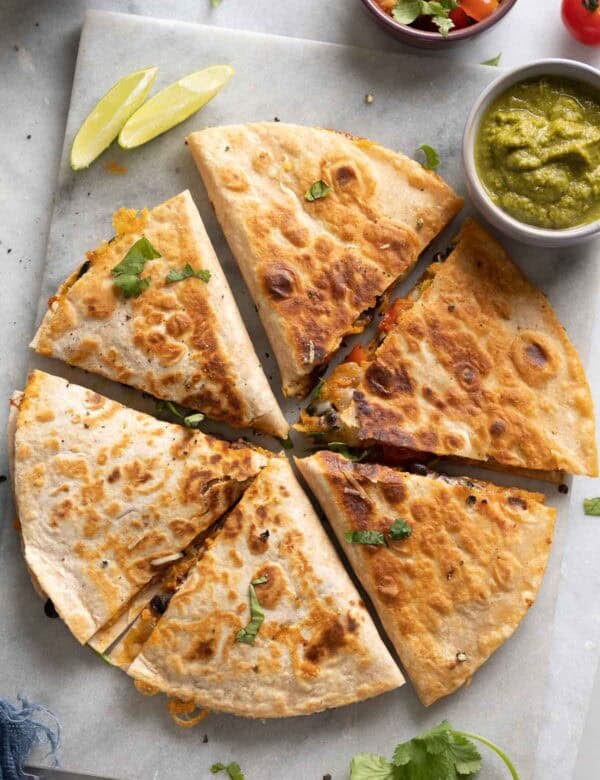 Two Sweet Potato & Black Bean Quesadillas arranged in circle and cut into 6 wedges on serving board with fresh cilantro and bowls of salsa on the side.